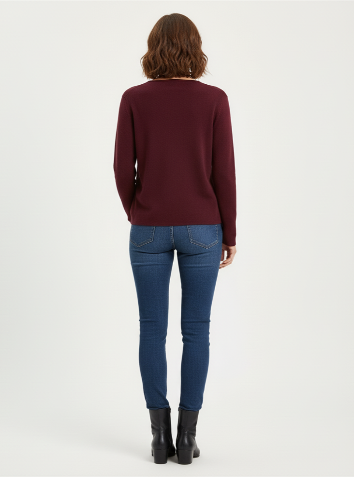 Person wearing a burgundy sweater and blue jeans on a white background