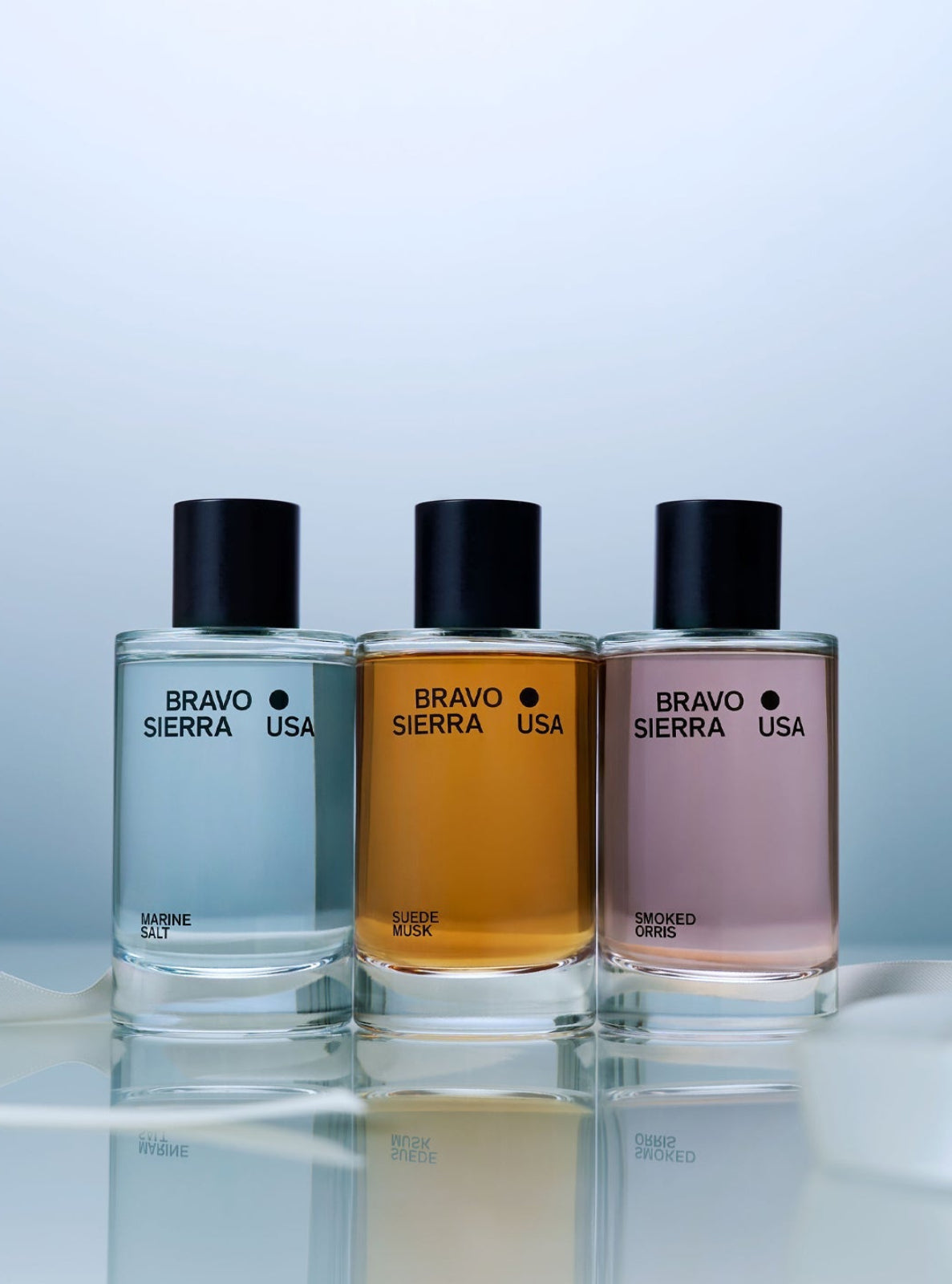 Three Bravo Sierra USA perfume bottles on a reflective surface with a light blue background