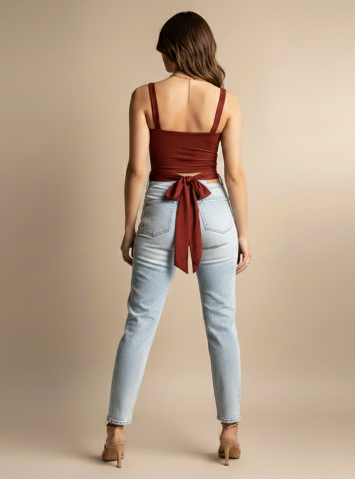 Woman wearing a red top and light blue jeans on a beige background