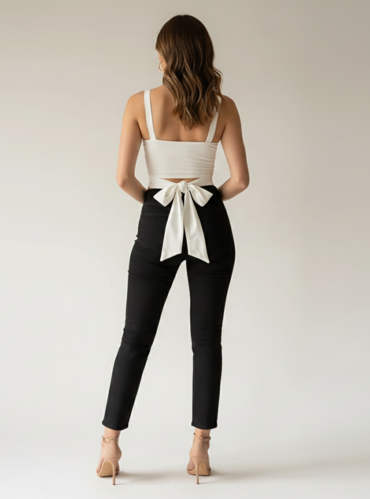 Woman wearing a white top with a bow and black pants on a plain background