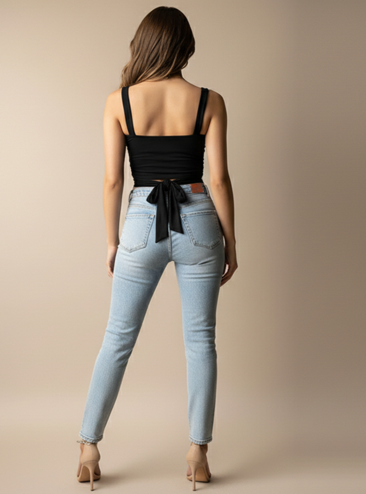 Woman wearing light blue jeans and a black top with a beige background