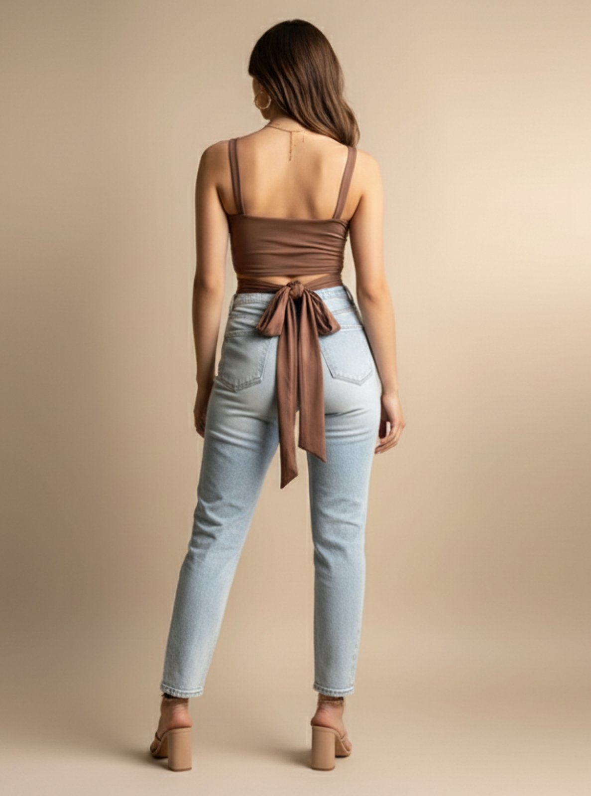 Woman wearing a brown top and light blue jeans on a beige background