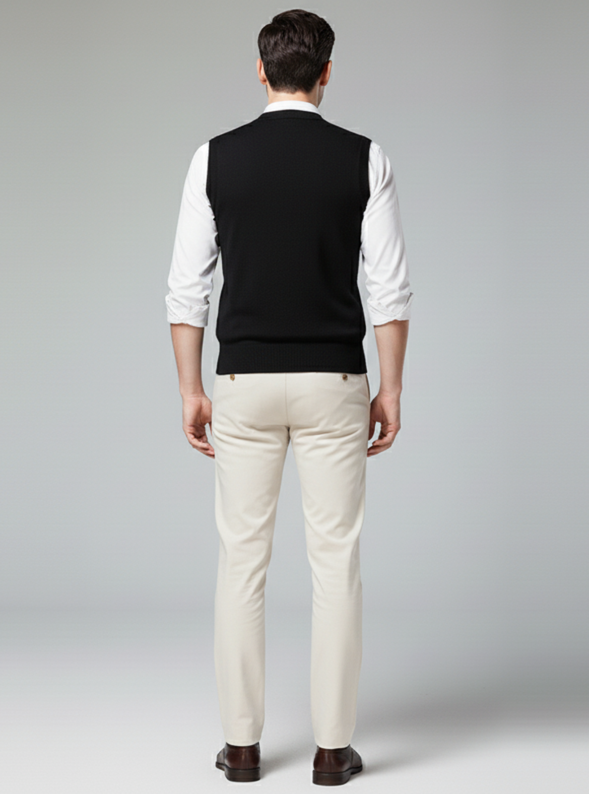 Man wearing a black vest over a white shirt with beige pants on a gray background