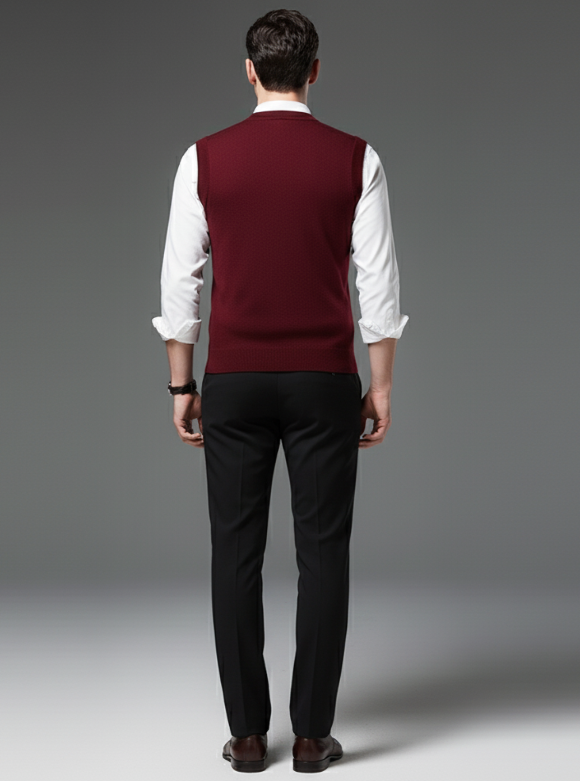 Man wearing a burgundy vest over a white shirt with black pants on a gray background
