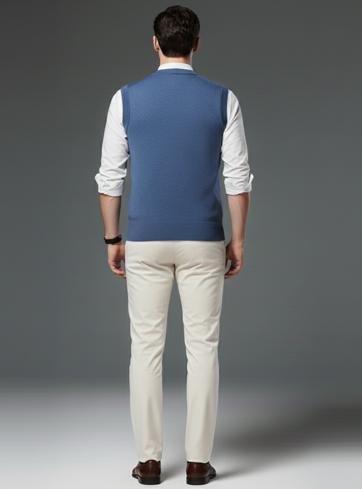 Man wearing a blue vest over a white shirt with beige pants on a gray background