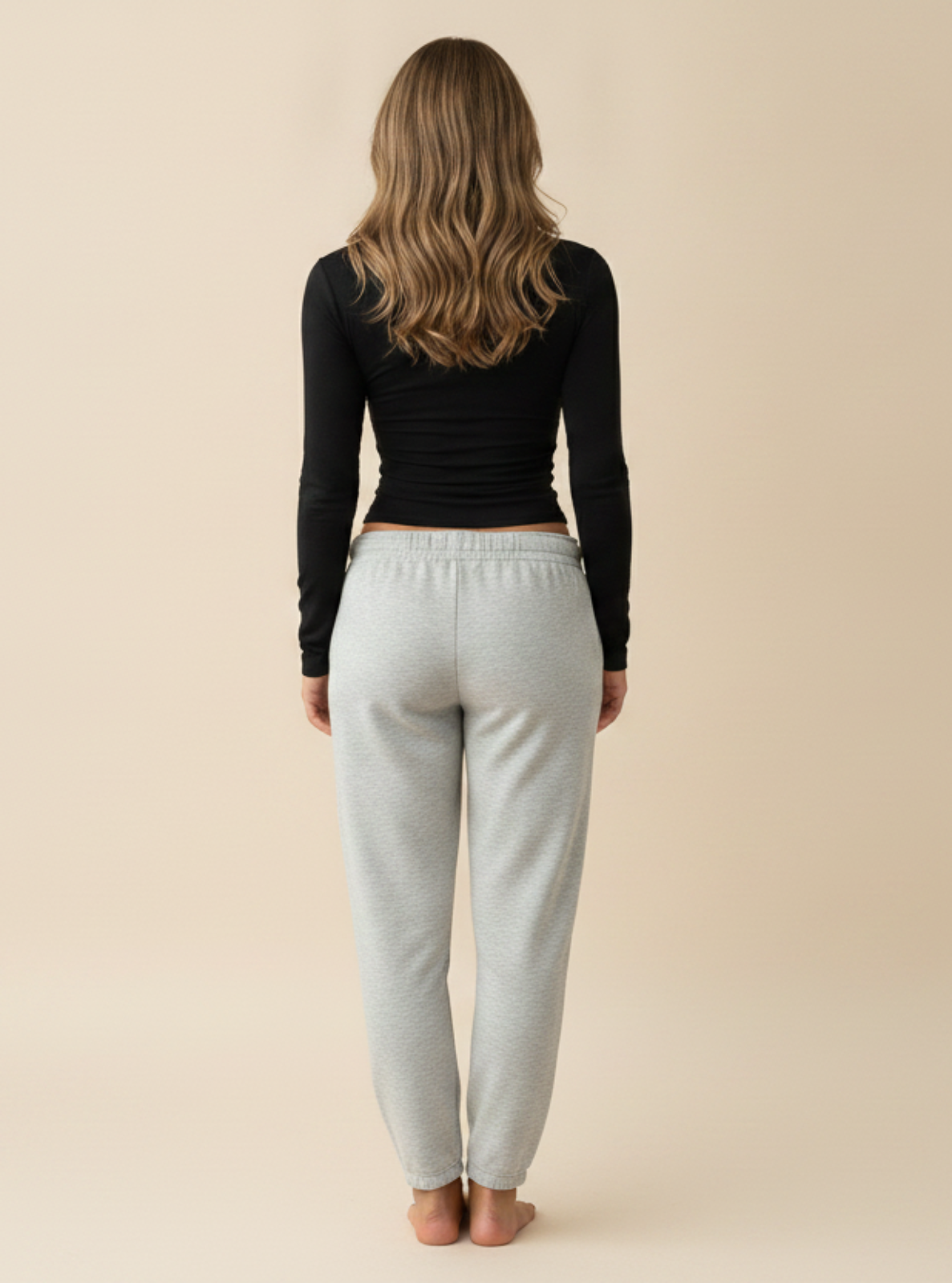 Person wearing a black long-sleeve top and light gray sweatpants on a beige background