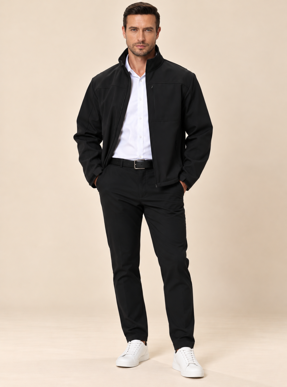 A man modeling a black zip-up jacket, white dress shirt, black trousers, and white sneakers against a solid beige studio background.