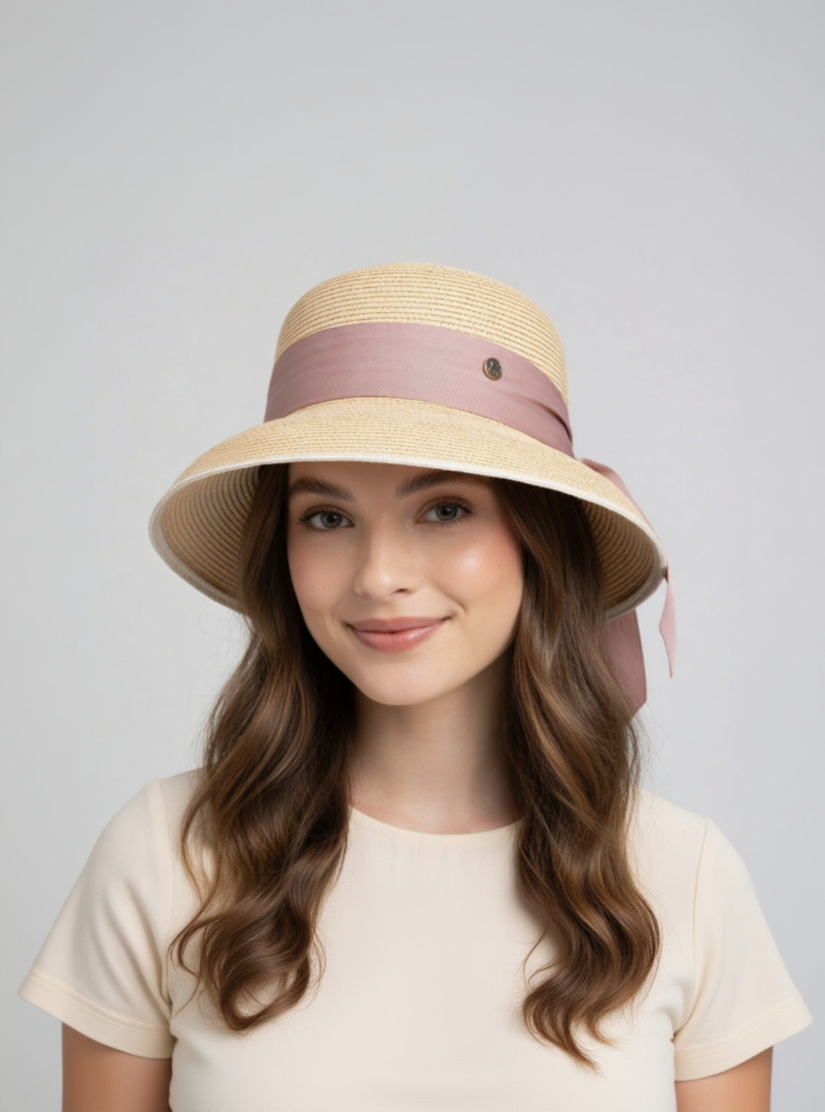 Woman wearing a straw hat with a pink band on a plain background