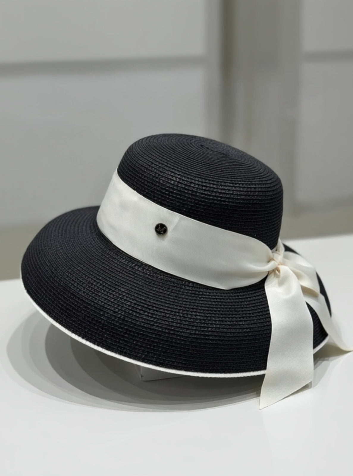 Black straw hat with a white ribbon on a white surface