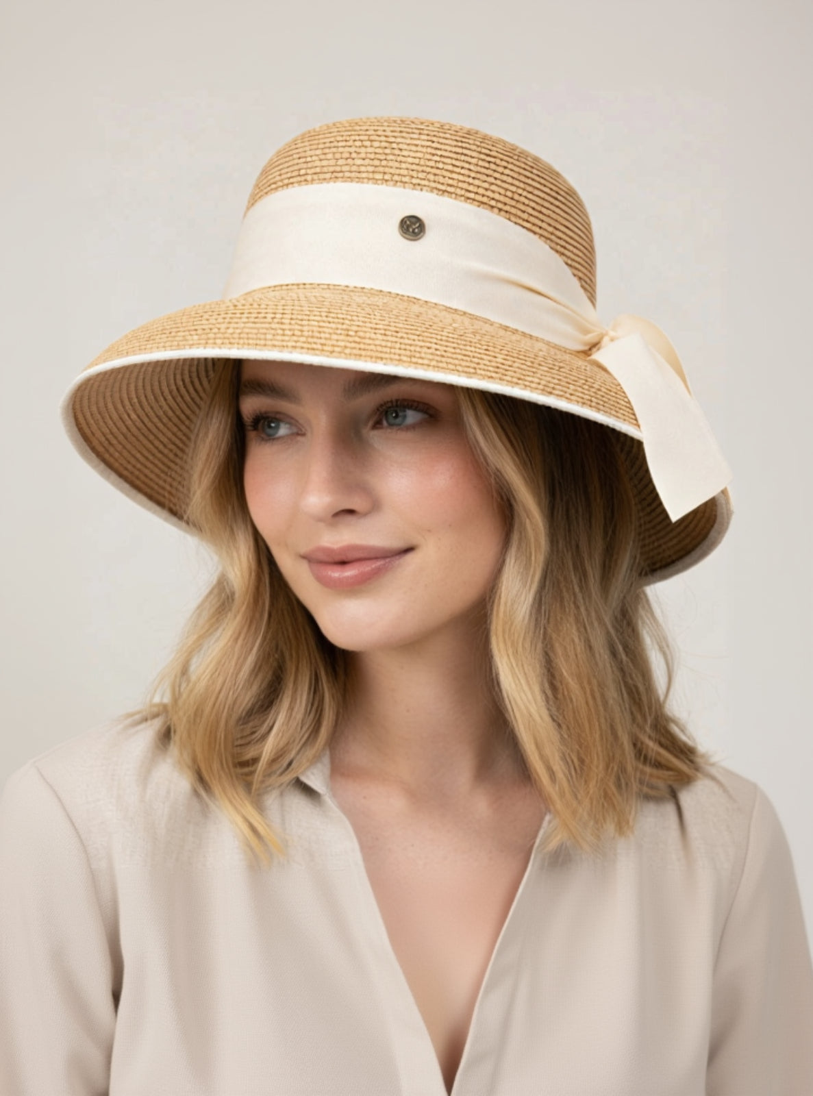 Woman wearing a beige sun hat with a white ribbon on a plain background
