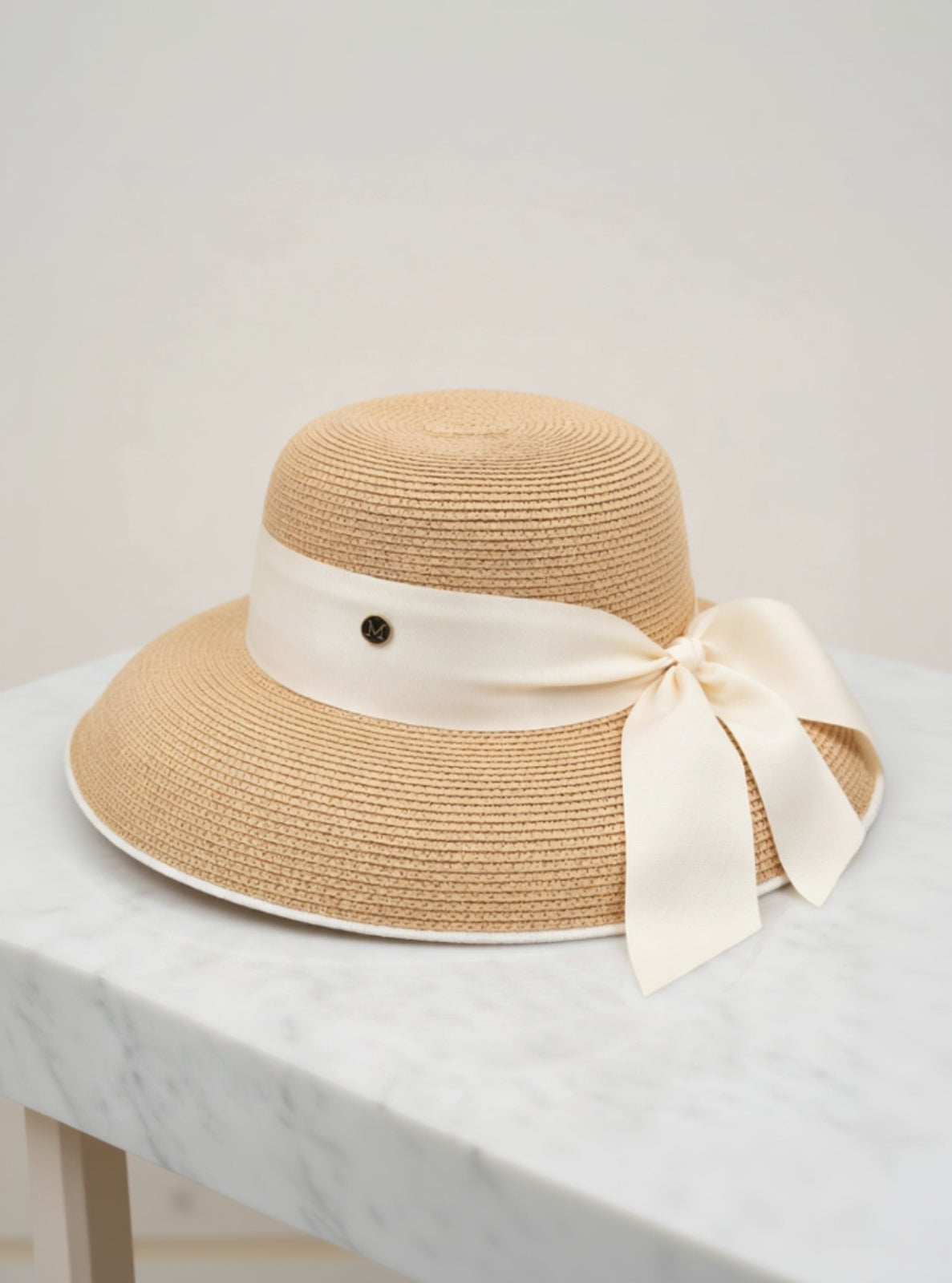 Beige straw hat with a white ribbon on a light gray surface