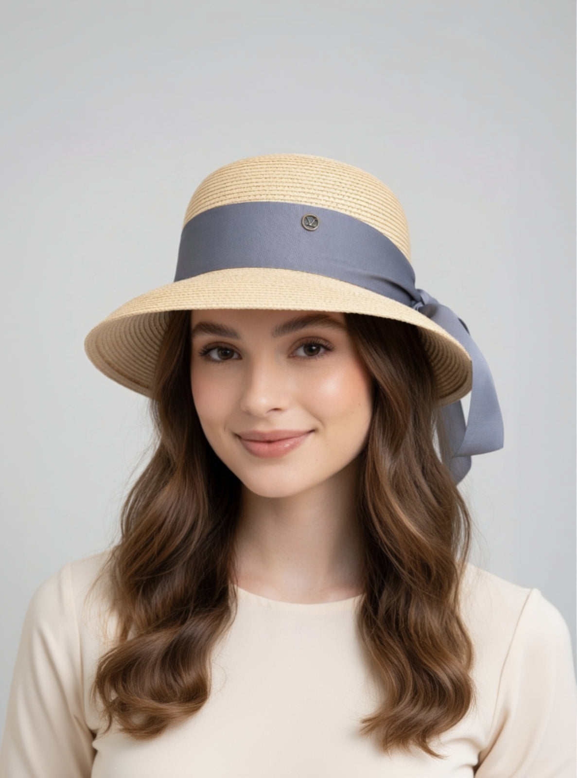 Woman wearing a straw hat with a blue ribbon on a gray background