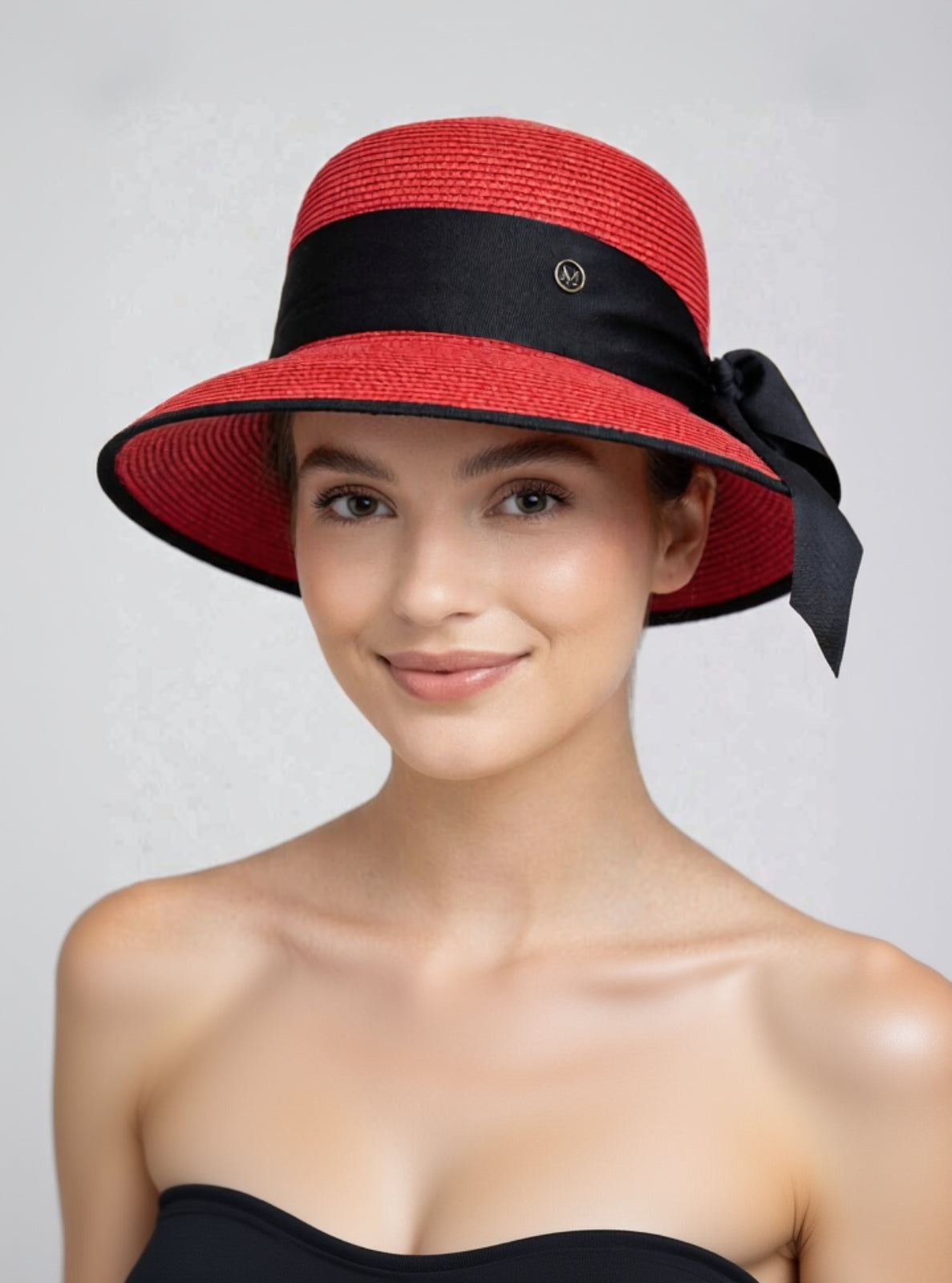 Red sun hat with a black band worn by a model on a light gray background