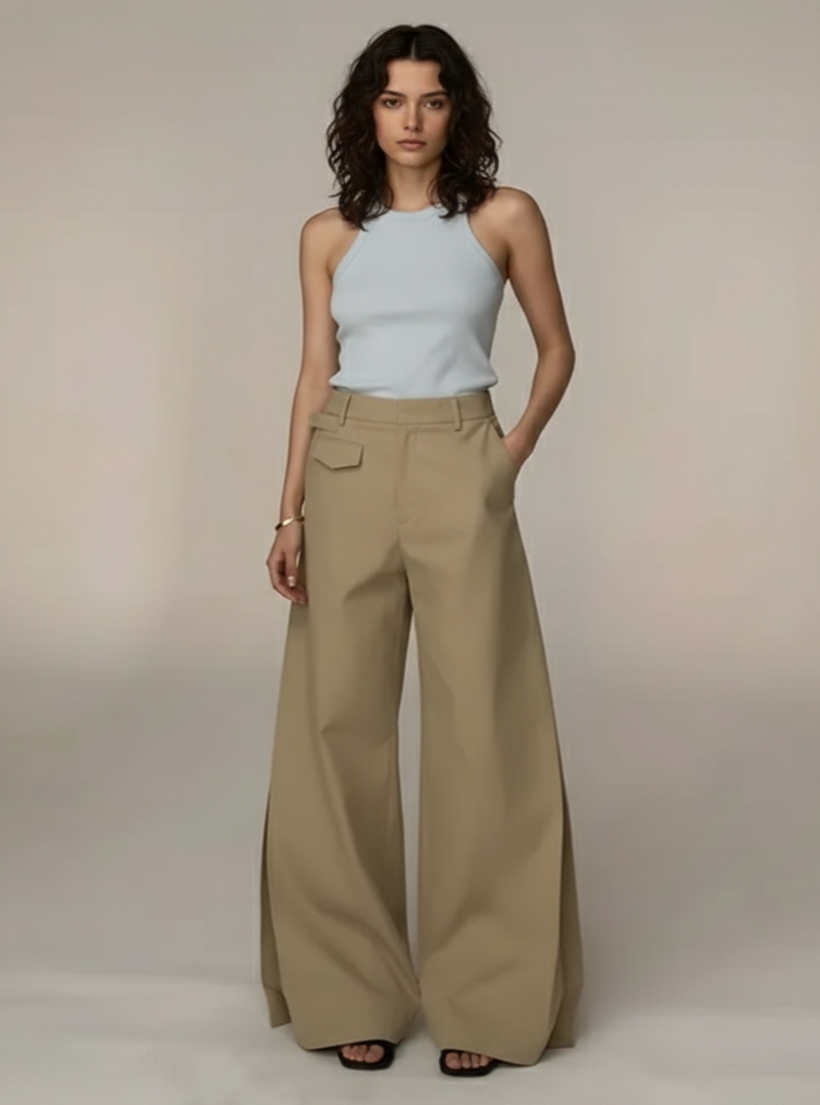 Woman wearing a light blue sleeveless top and beige wide-leg pants against a neutral background