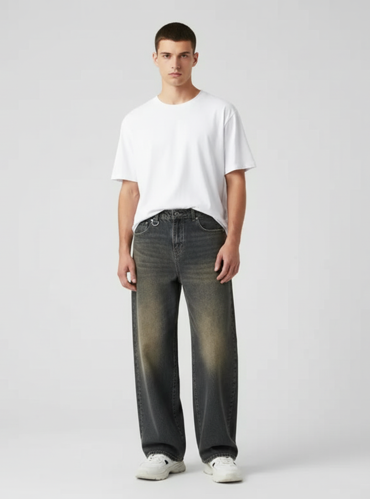 Man wearing a white t-shirt and dark jeans on a light gray background