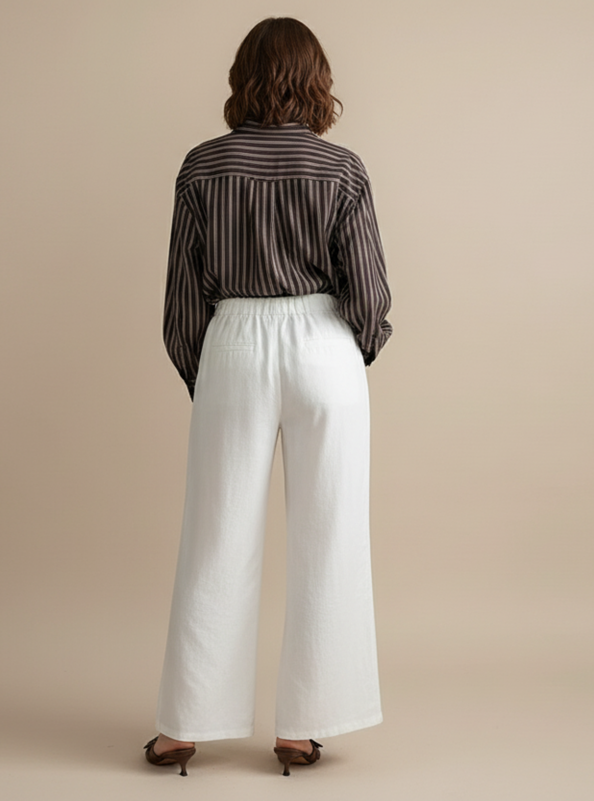 Person wearing a striped shirt and white pants on a beige background