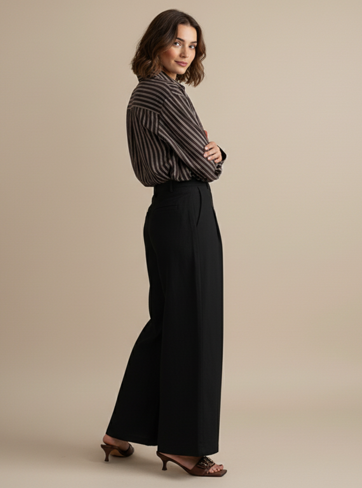Woman wearing a striped shirt and black wide-leg pants on a beige background