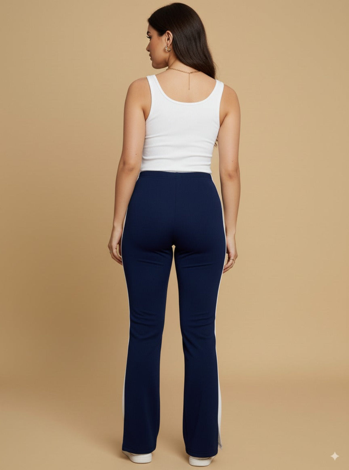 Woman wearing a white tank top and navy blue pants on a beige background