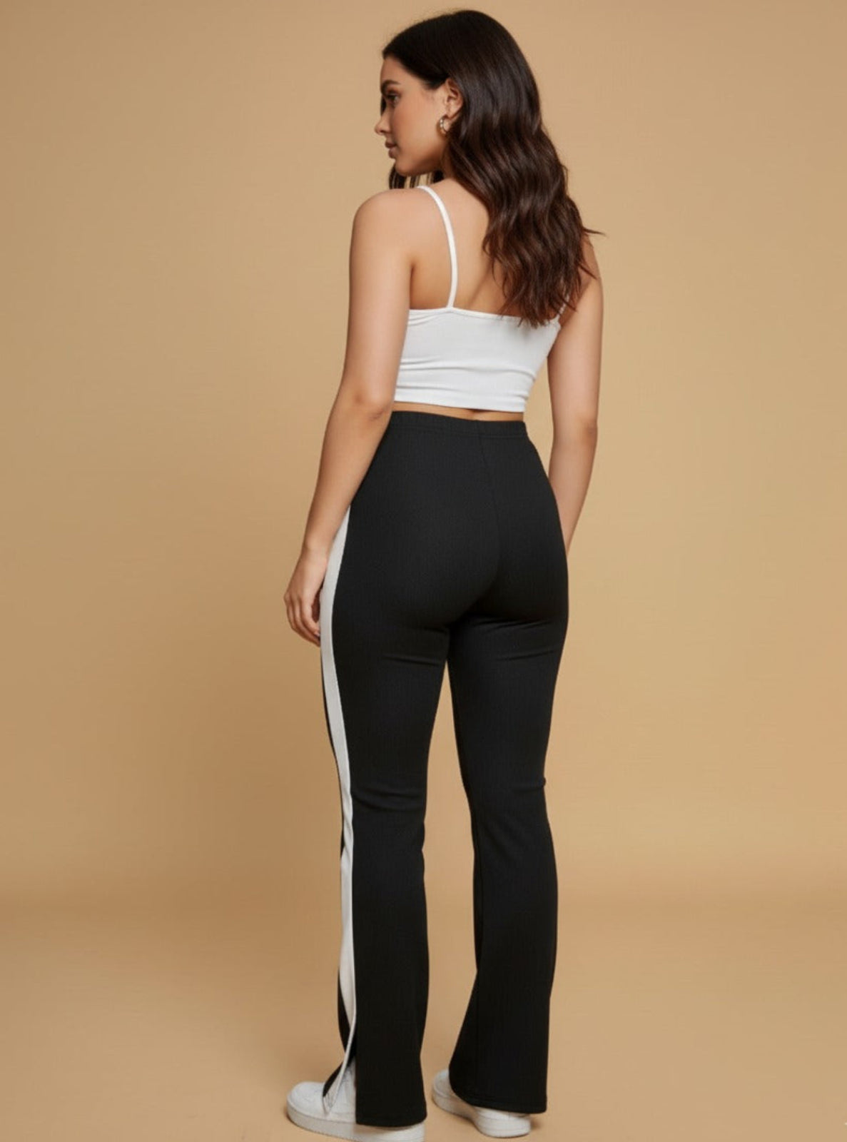 Woman wearing a white crop top and black pants with a white stripe on a beige background