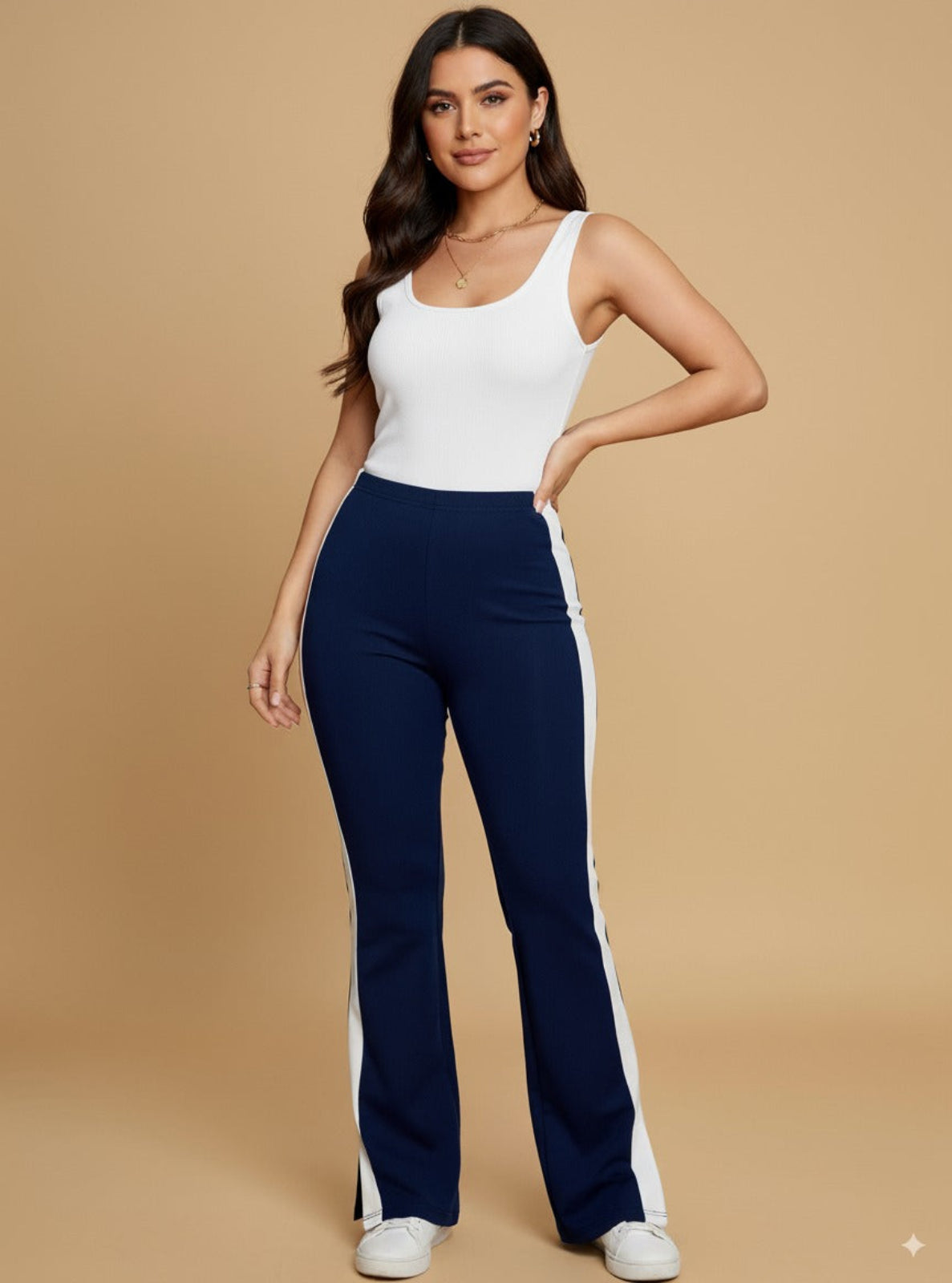 Woman wearing a white tank top and navy pants with a beige background