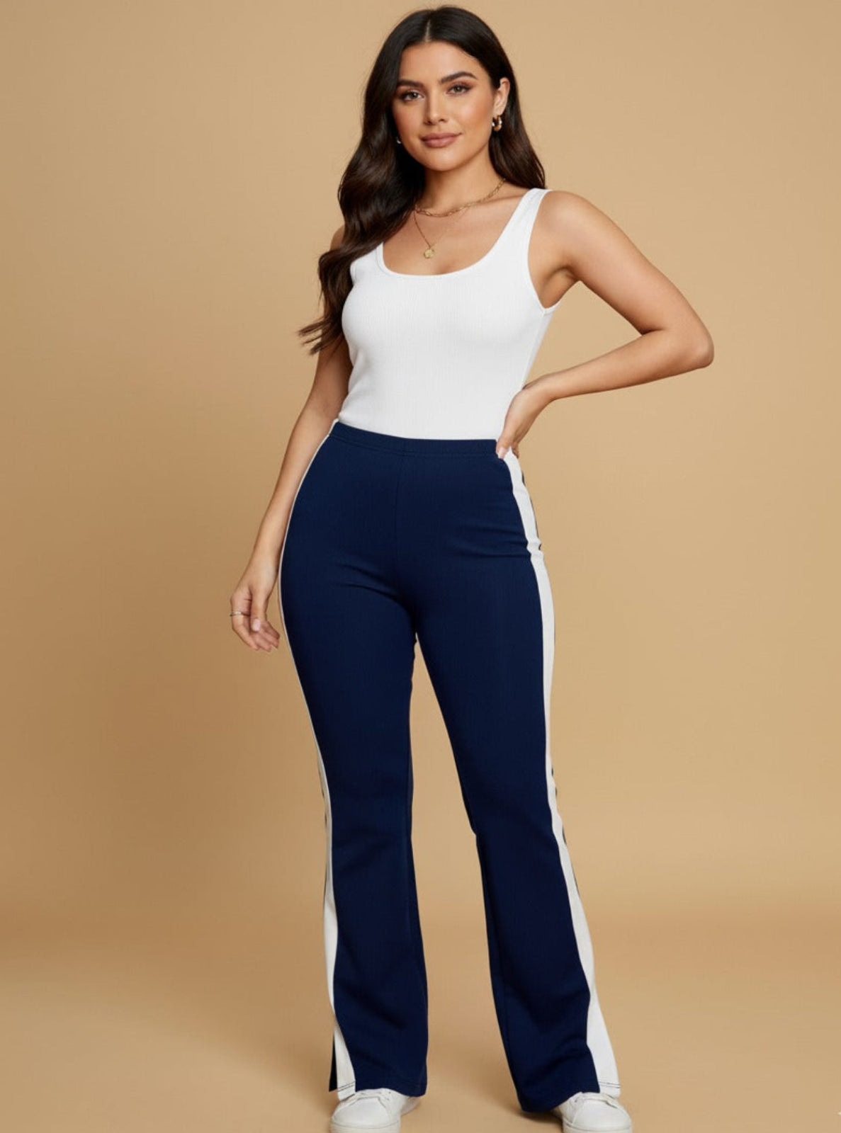 Woman wearing a white tank top and navy pants with a beige background