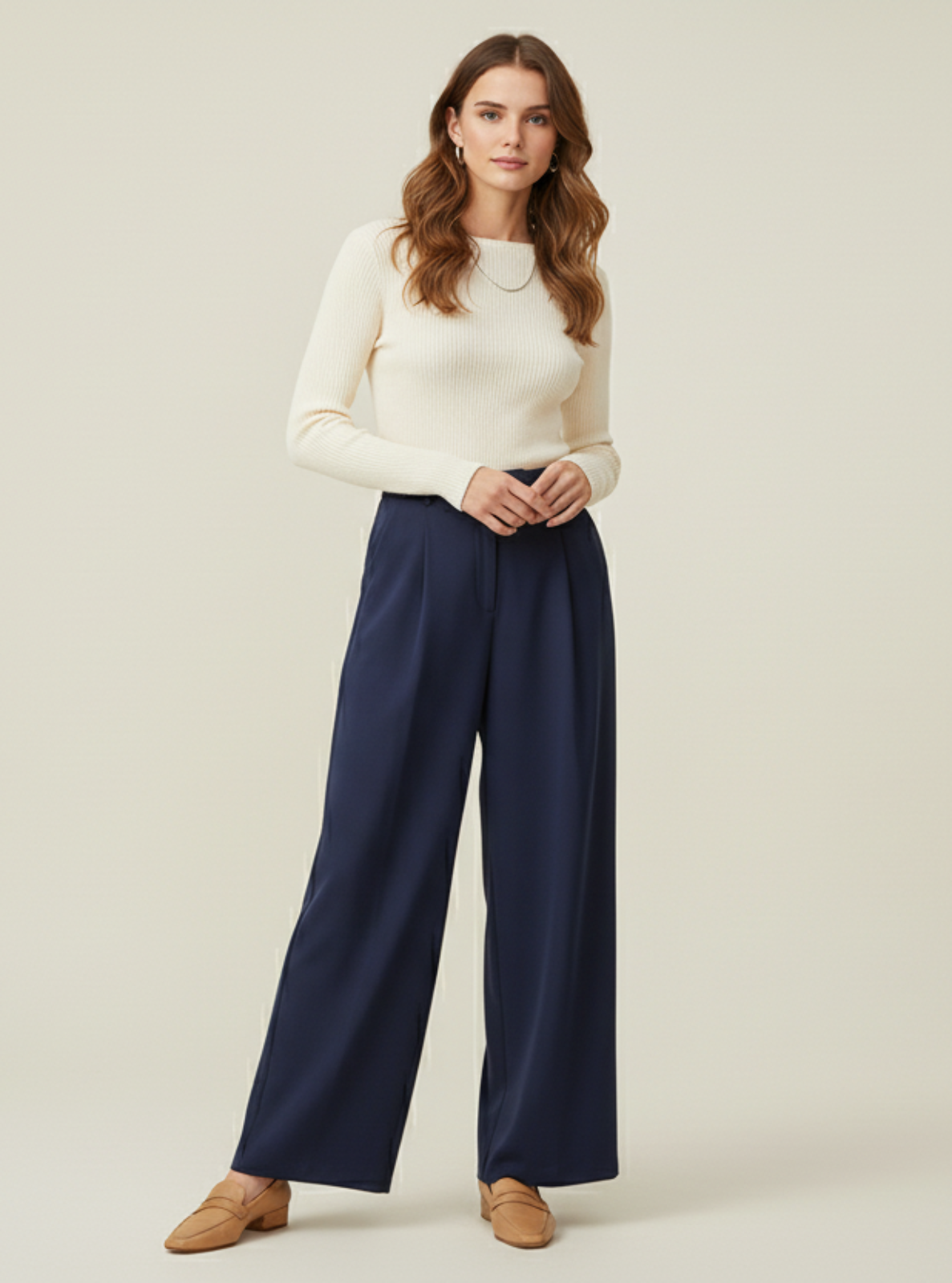 Woman wearing a white sweater and navy pants on a plain background