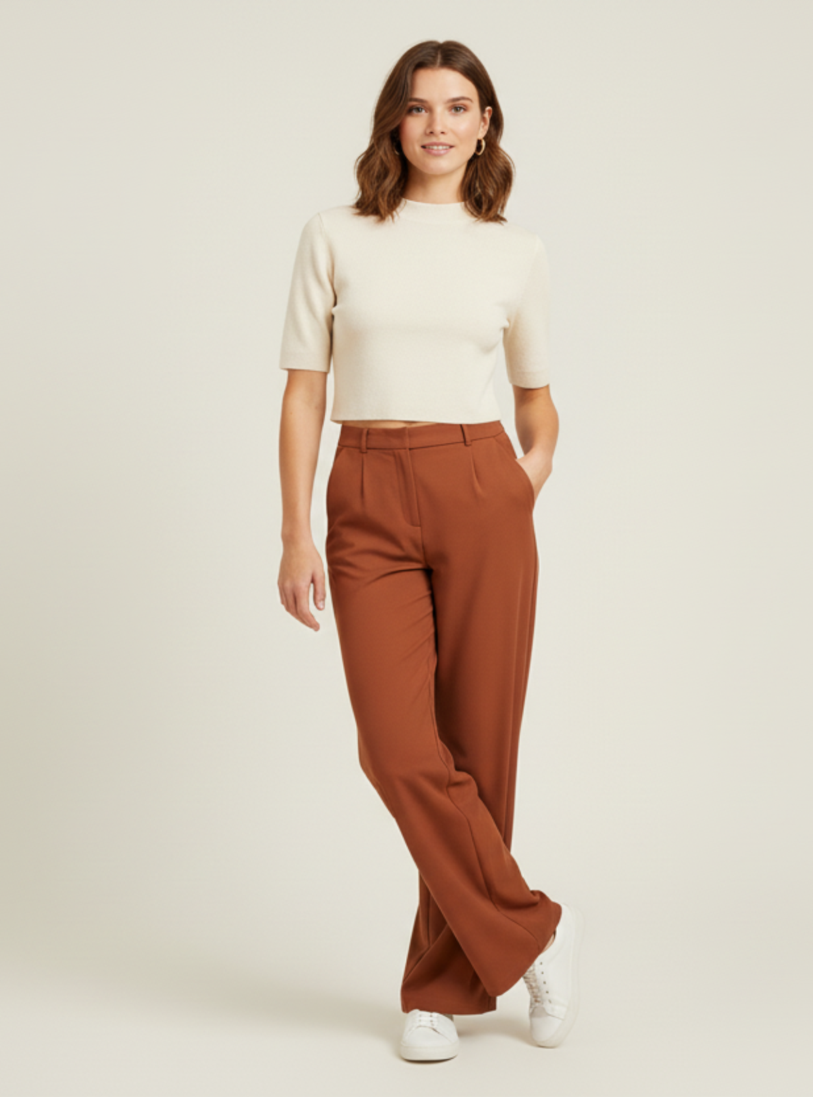 Woman wearing a white top and brown pants on a light beige background