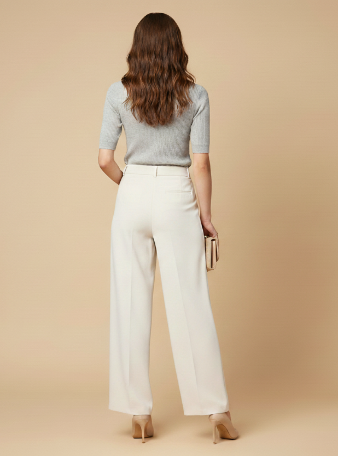 Woman wearing a light gray top and white pants against a beige background