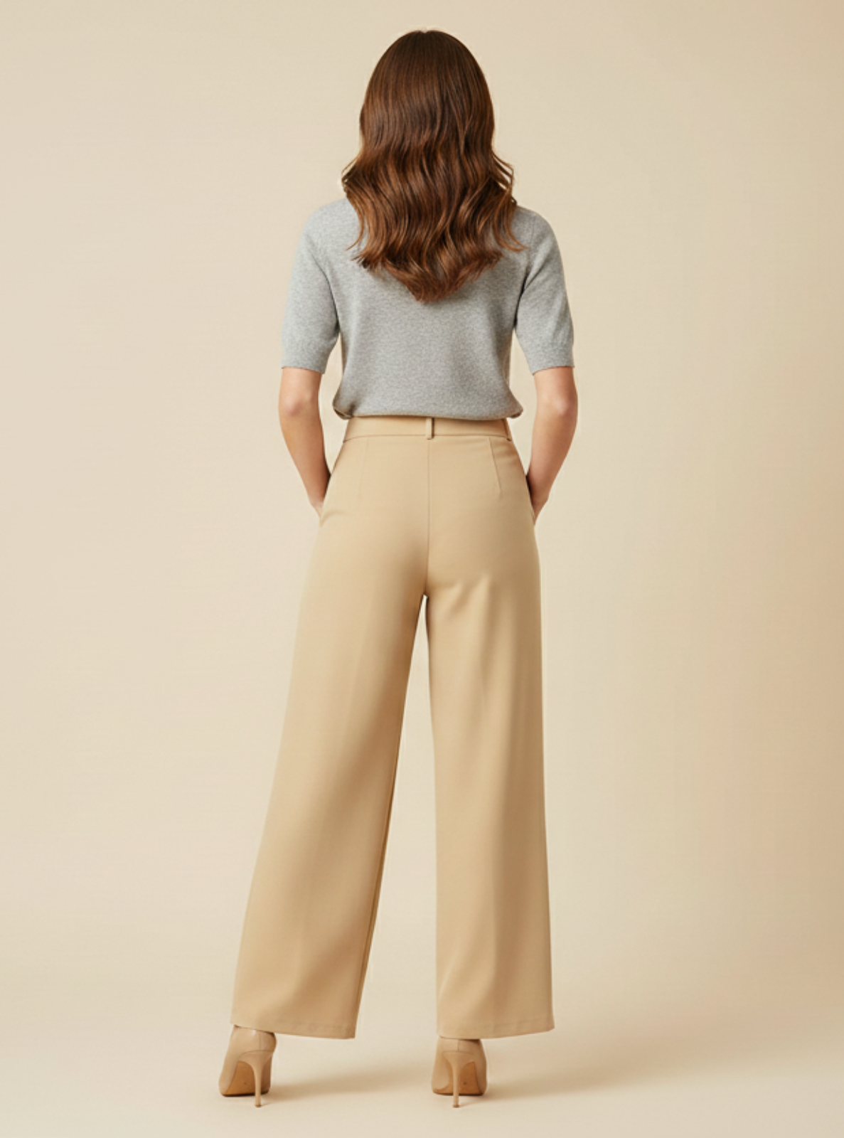 Woman wearing a light gray top and beige pants on a beige background