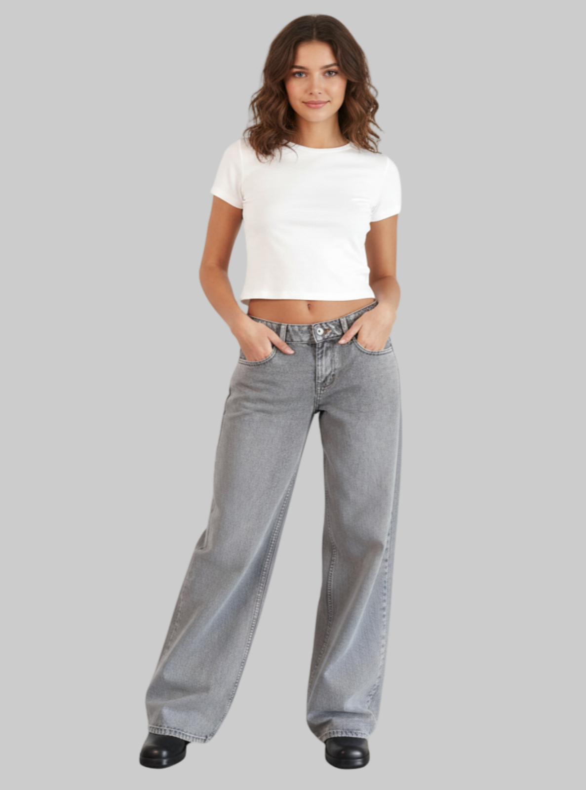 Woman wearing a white crop top and gray jeans on a white background
