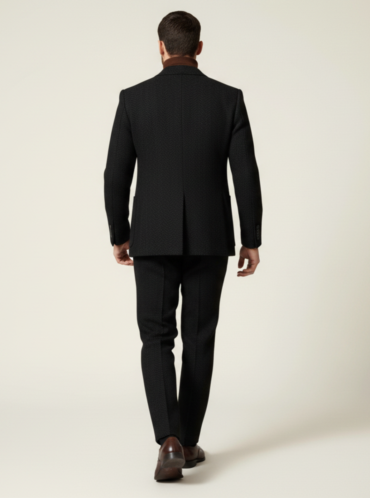 Man wearing a black suit standing against a plain background