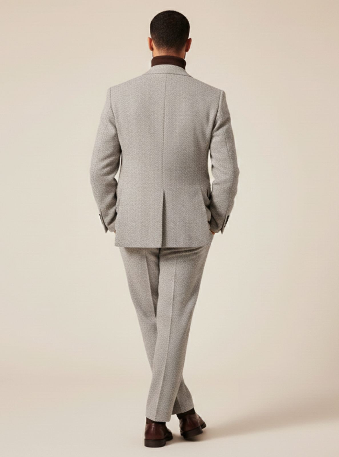 Man wearing a gray suit standing against a beige background