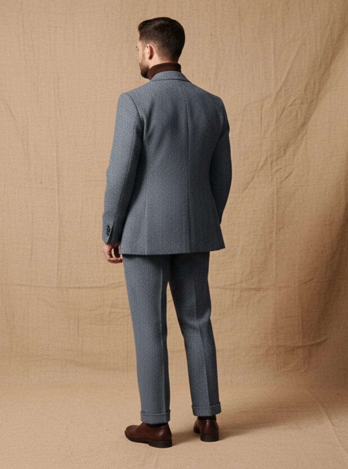 Man in a gray suit standing in front of a beige backdrop in a studio setting.