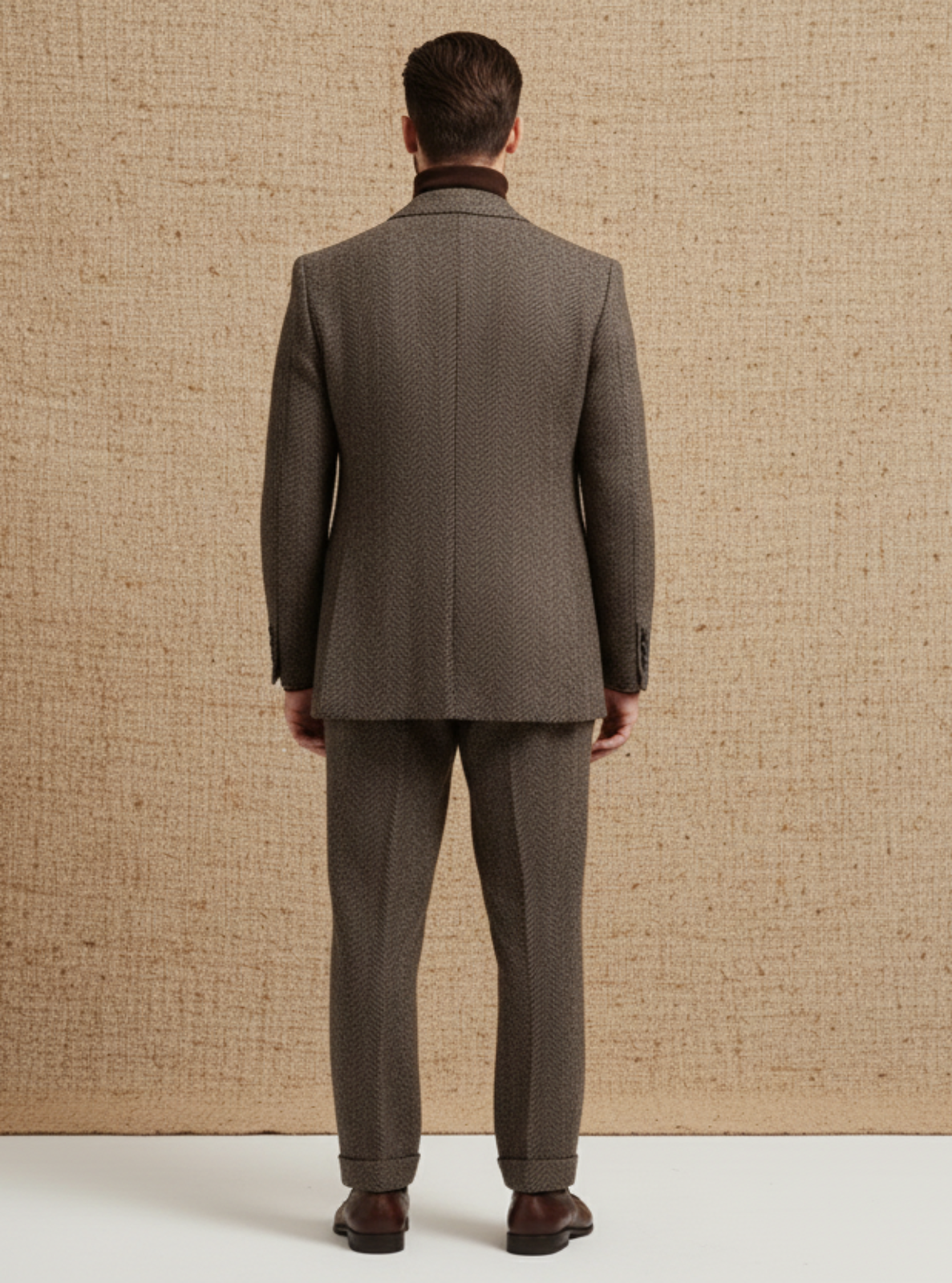 Man wearing a brown suit standing in front of a textured beige backdrop