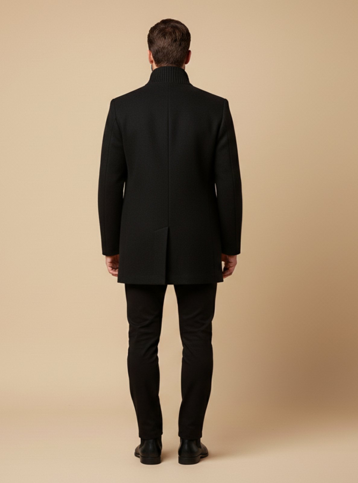 Man wearing a black suit standing against a beige background