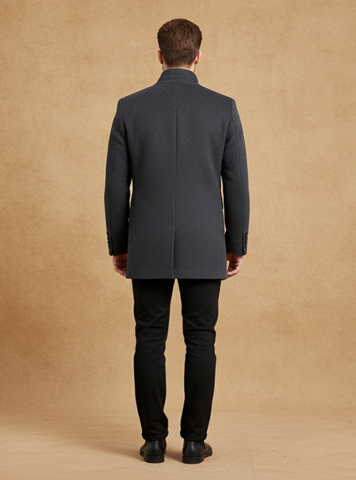Man wearing a dark gray coat and black pants against a beige backdrop