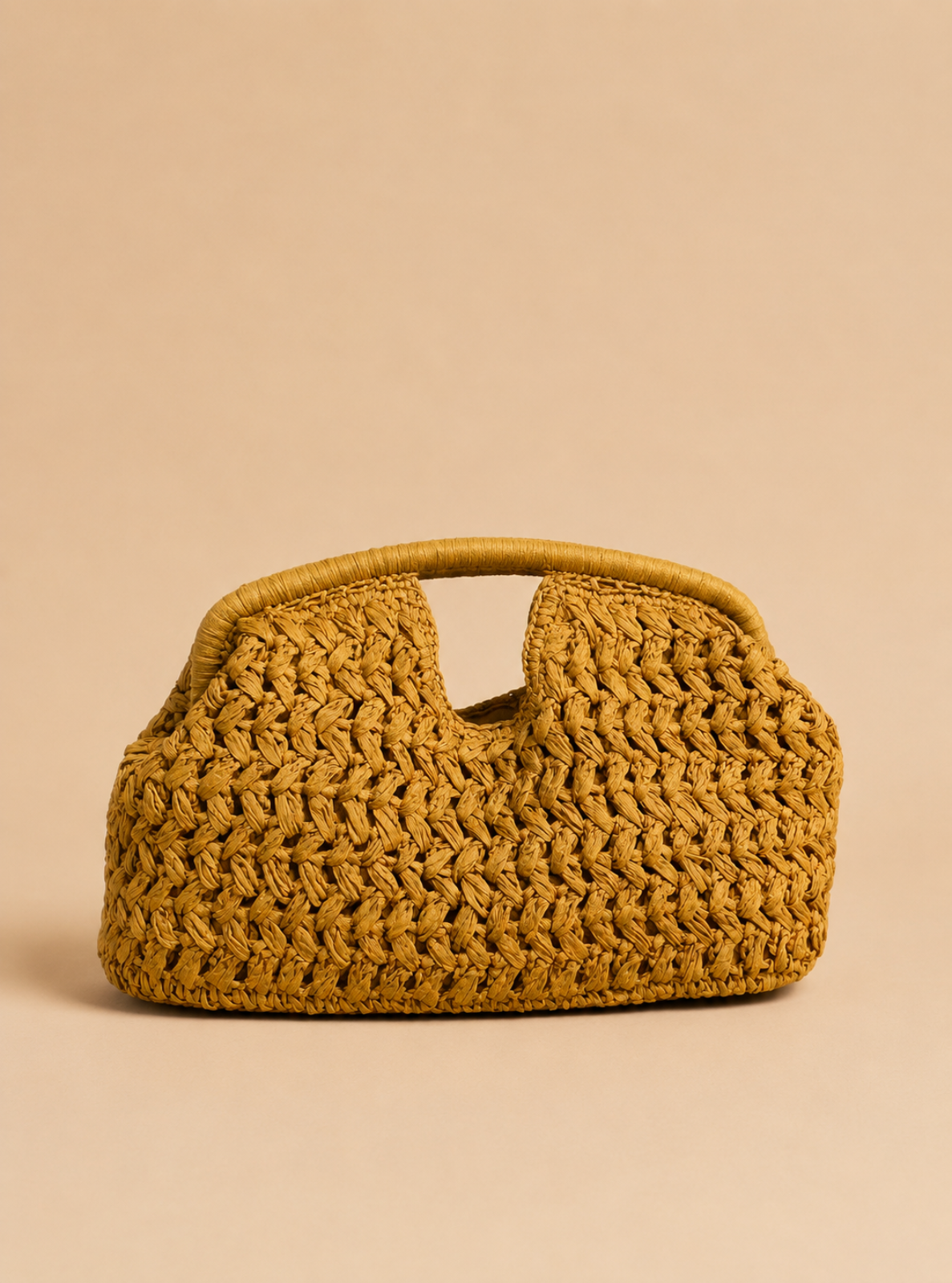 A small woven straw handbag in a warm mustard yellow color, featuring a curved top handle and a slouchy, textured body, set against a solid beige background.