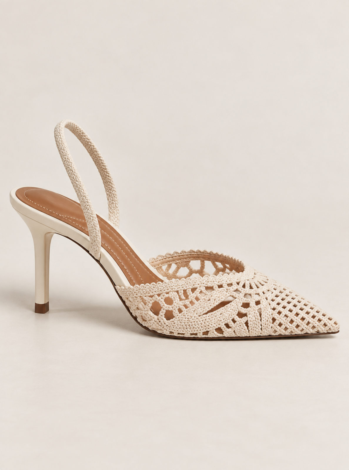 A single women's slingback high heel shoe with a pointed toe and openwork crochet detailing, shown in a warm cream or off-white color on a light beige studio background.