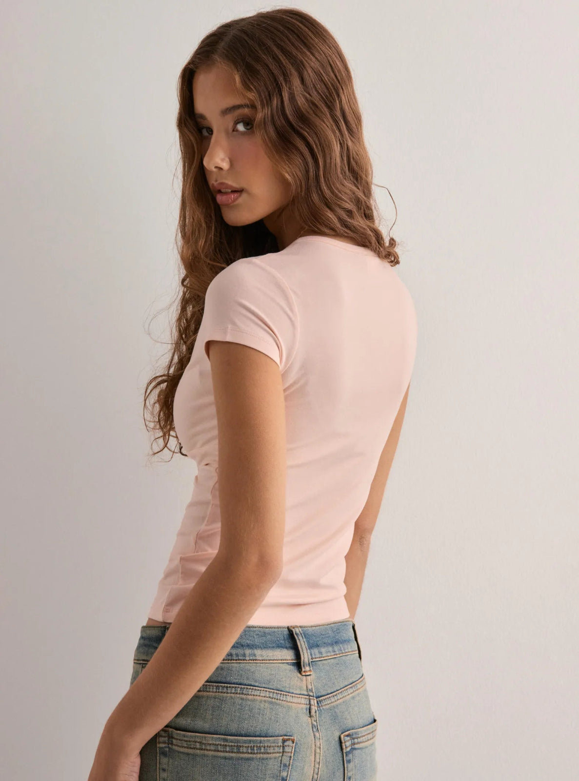 Woman wearing a pink t-shirt and blue jeans against a plain background