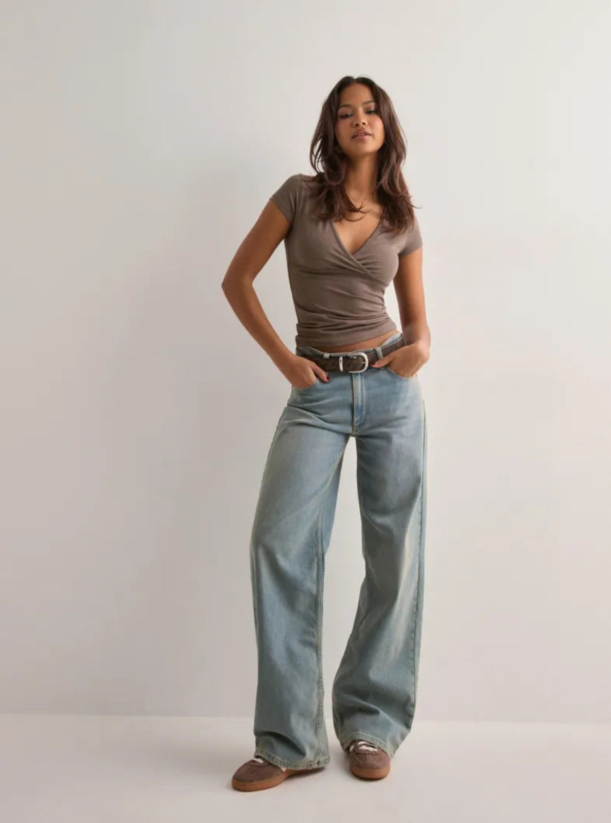 Woman wearing a brown top and light blue jeans against a white background