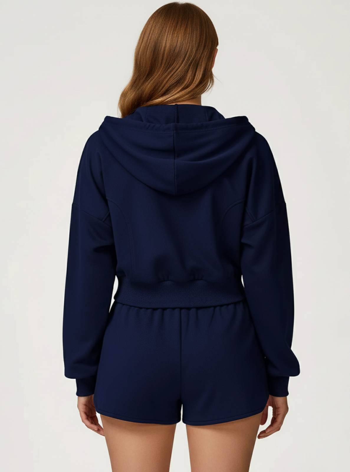 Person wearing a navy blue hoodie and shorts set on a light gray background