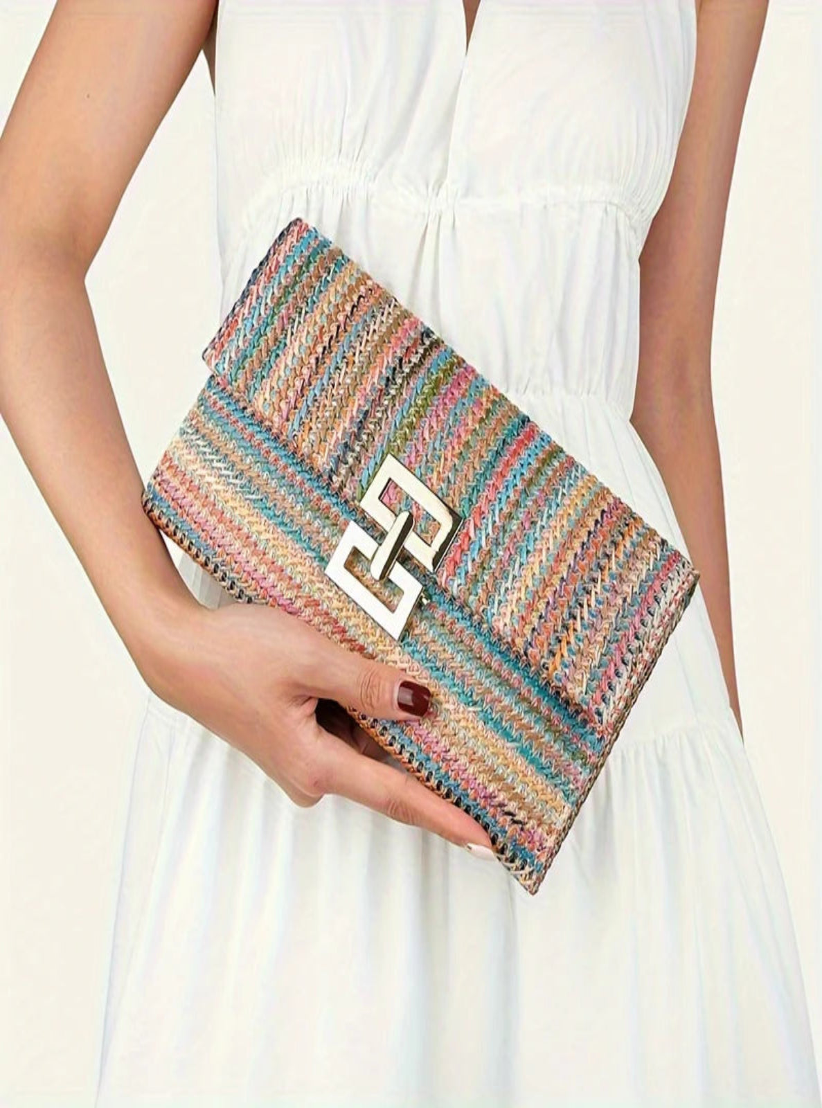 Multicolored striped clutch with a logo held by a person wearing a white dress.