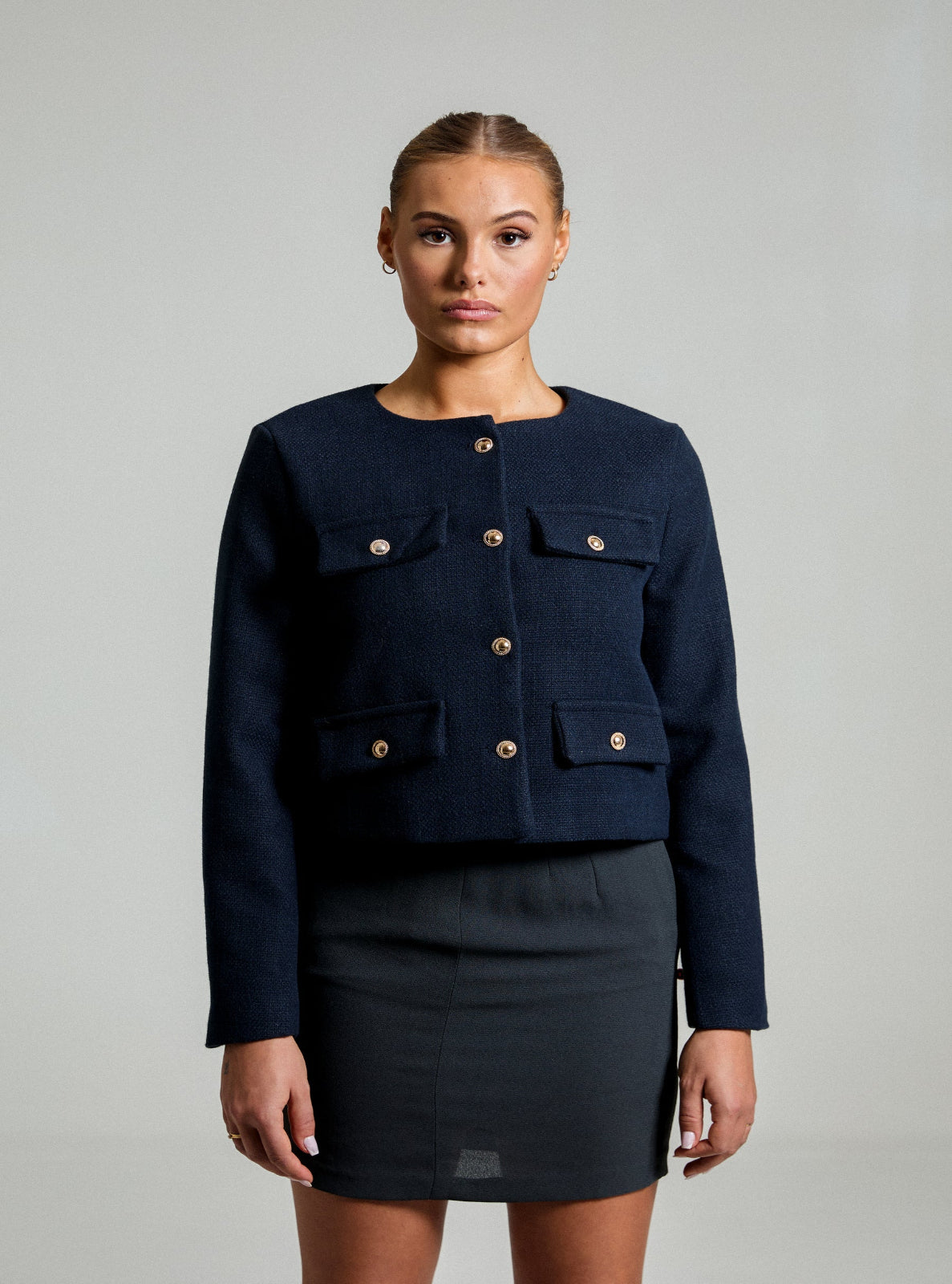 Model wearing a a navy blue textured Jacket and a gray pencil skirt in front of a white background 