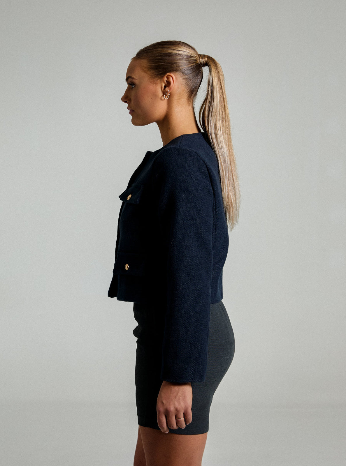 Side profile of model wearing a a navy blue textured Jacket with a gray pencil skirt in front of a white background
