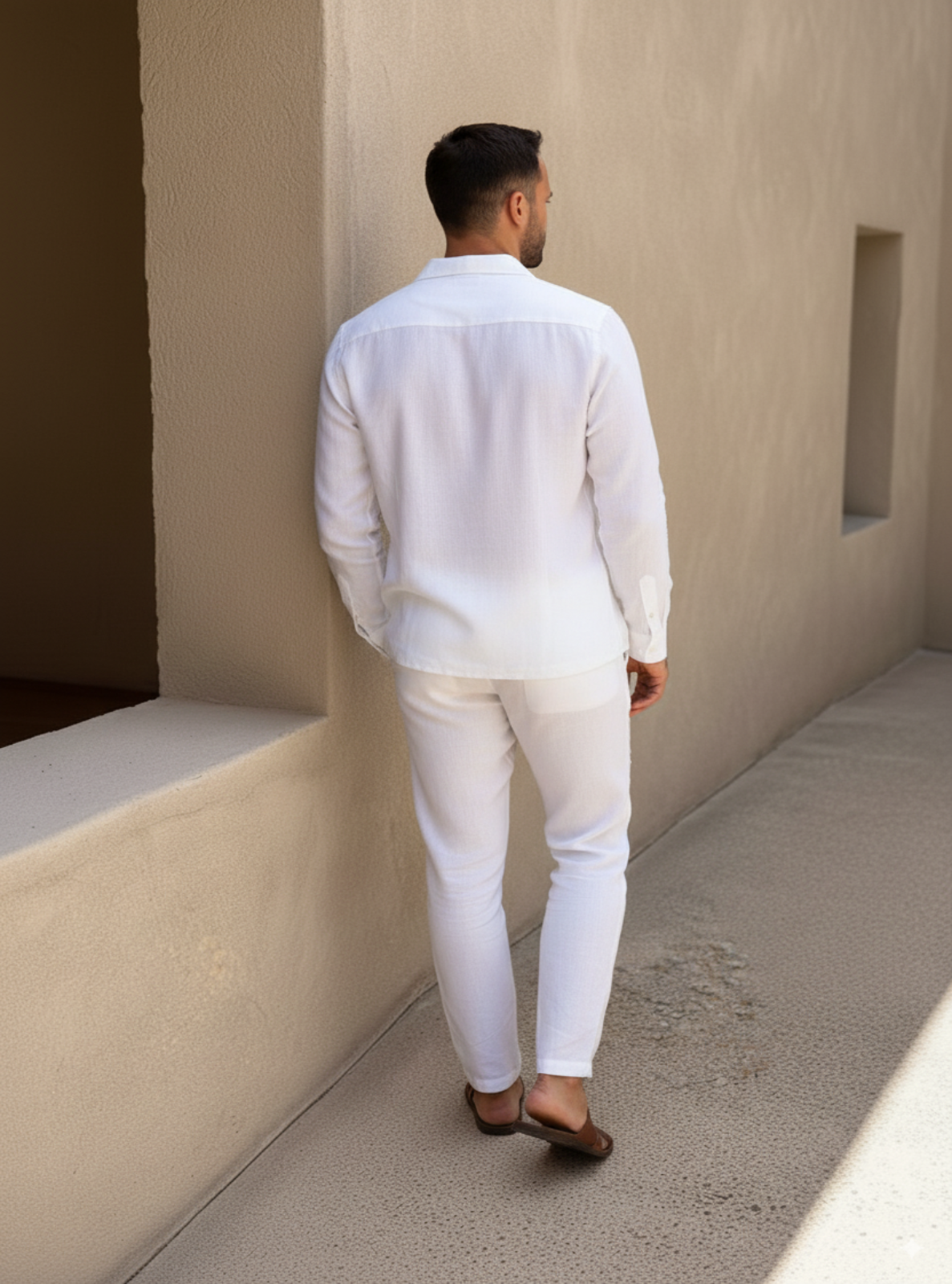 Man in a white outfit standing against a beige wall.