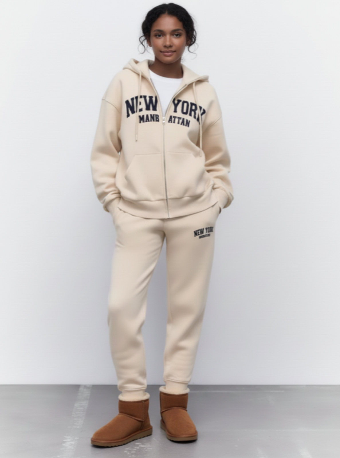 Person wearing a beige 'New York' hoodie and sweatpants with brown boots on a white background