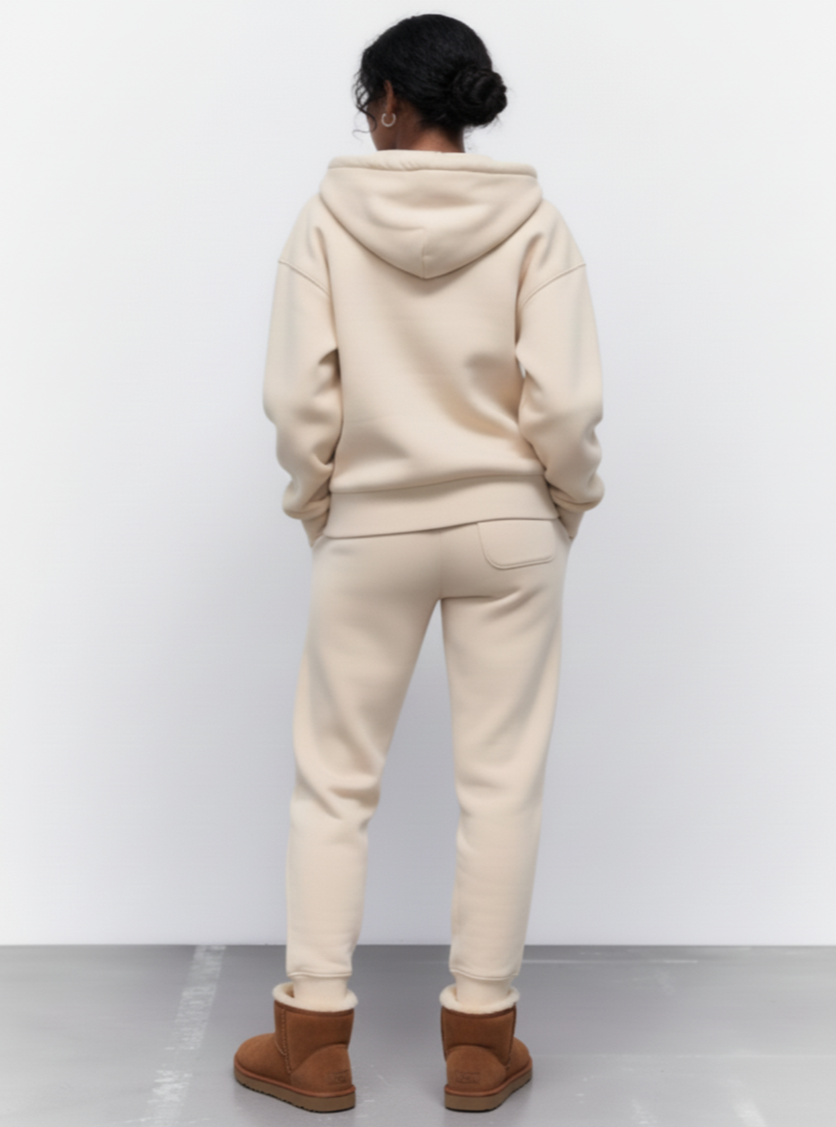 Person wearing a beige hoodie and pants with brown boots on a white background