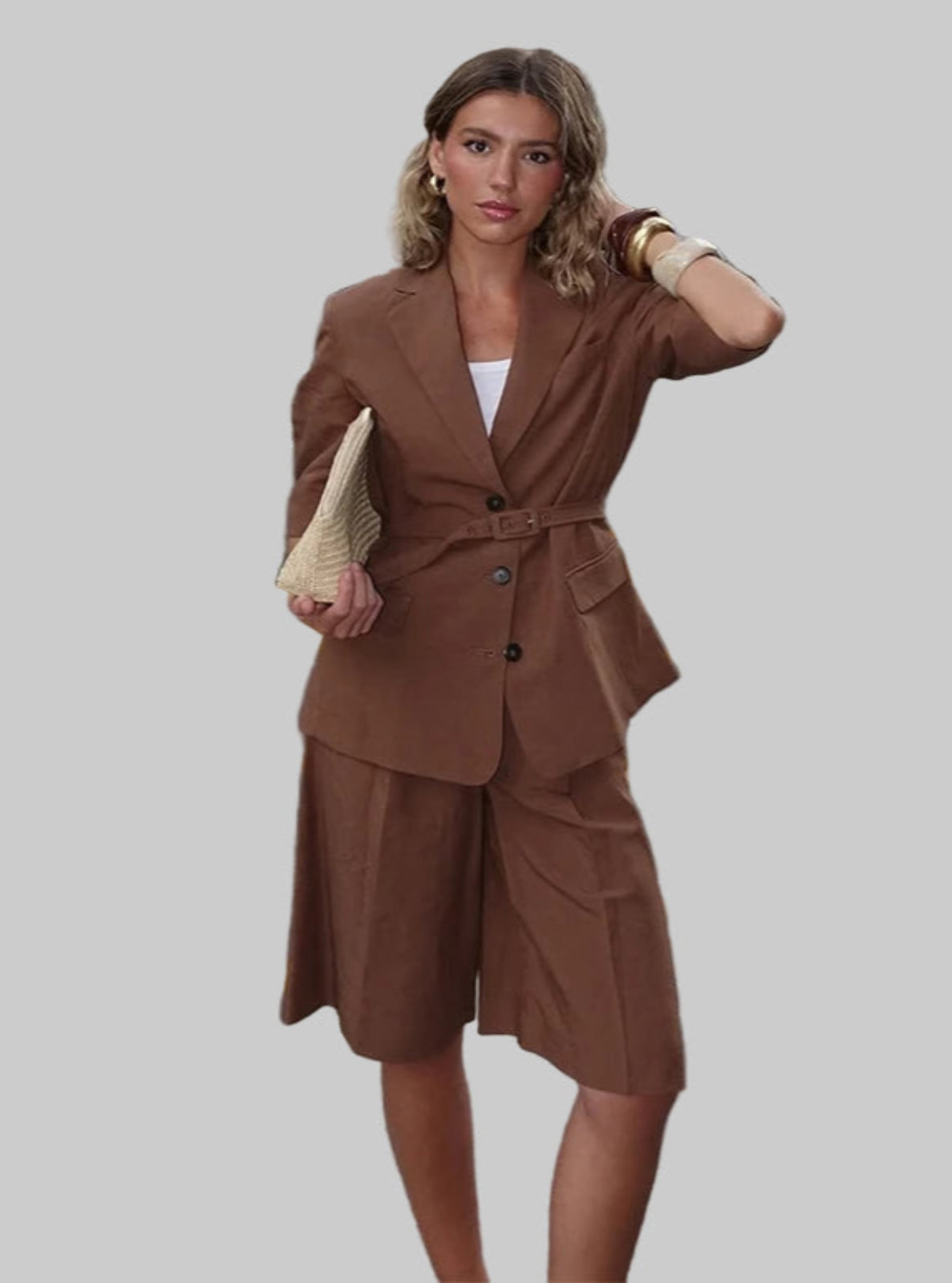 Woman in a brown outfit standing in front of a white wall.