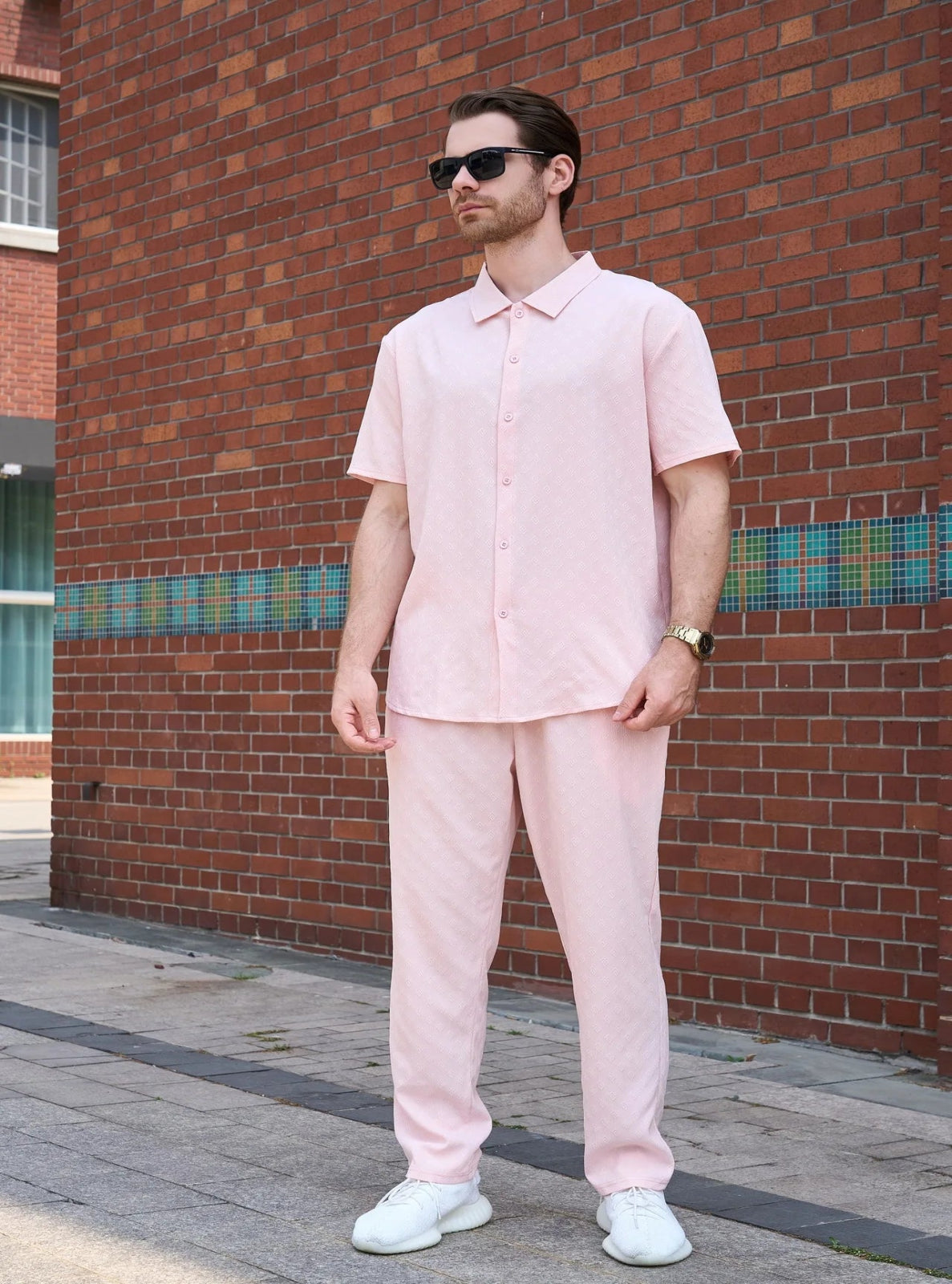 Man wearing a light pink outfit standing against a brick wall.