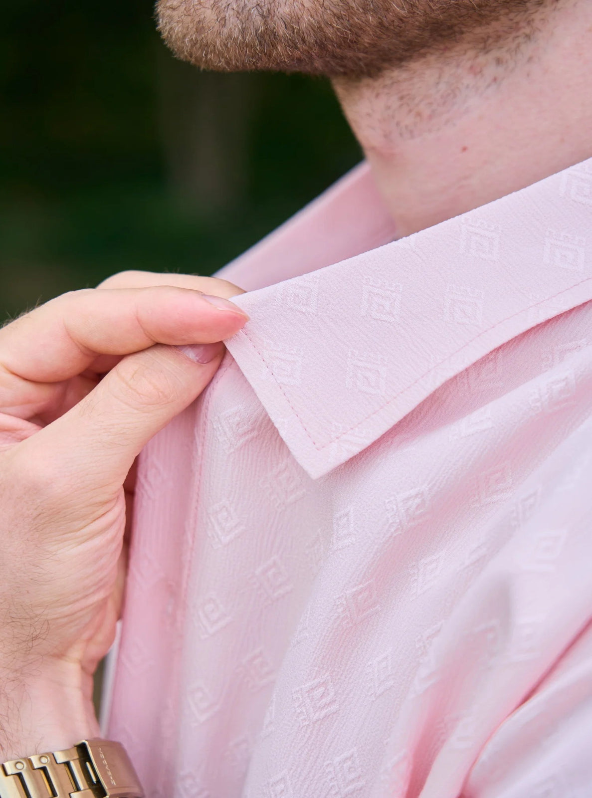 Person adjusting the collar of a light pink shirt with a blurred background